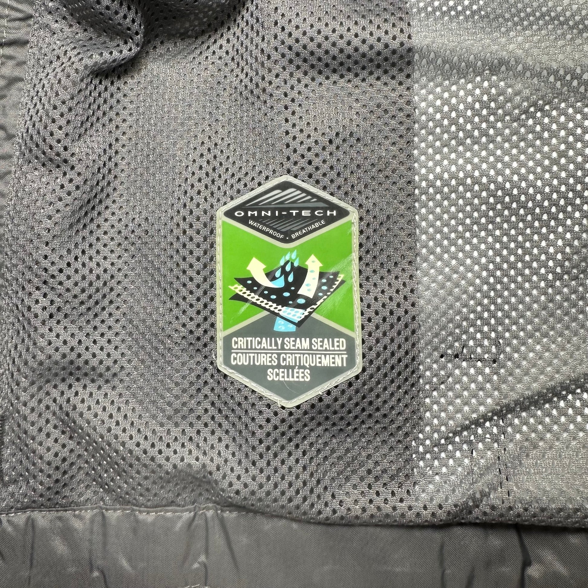 Close-up of a gray textured fabric with a green and white logo patch on a jacket.